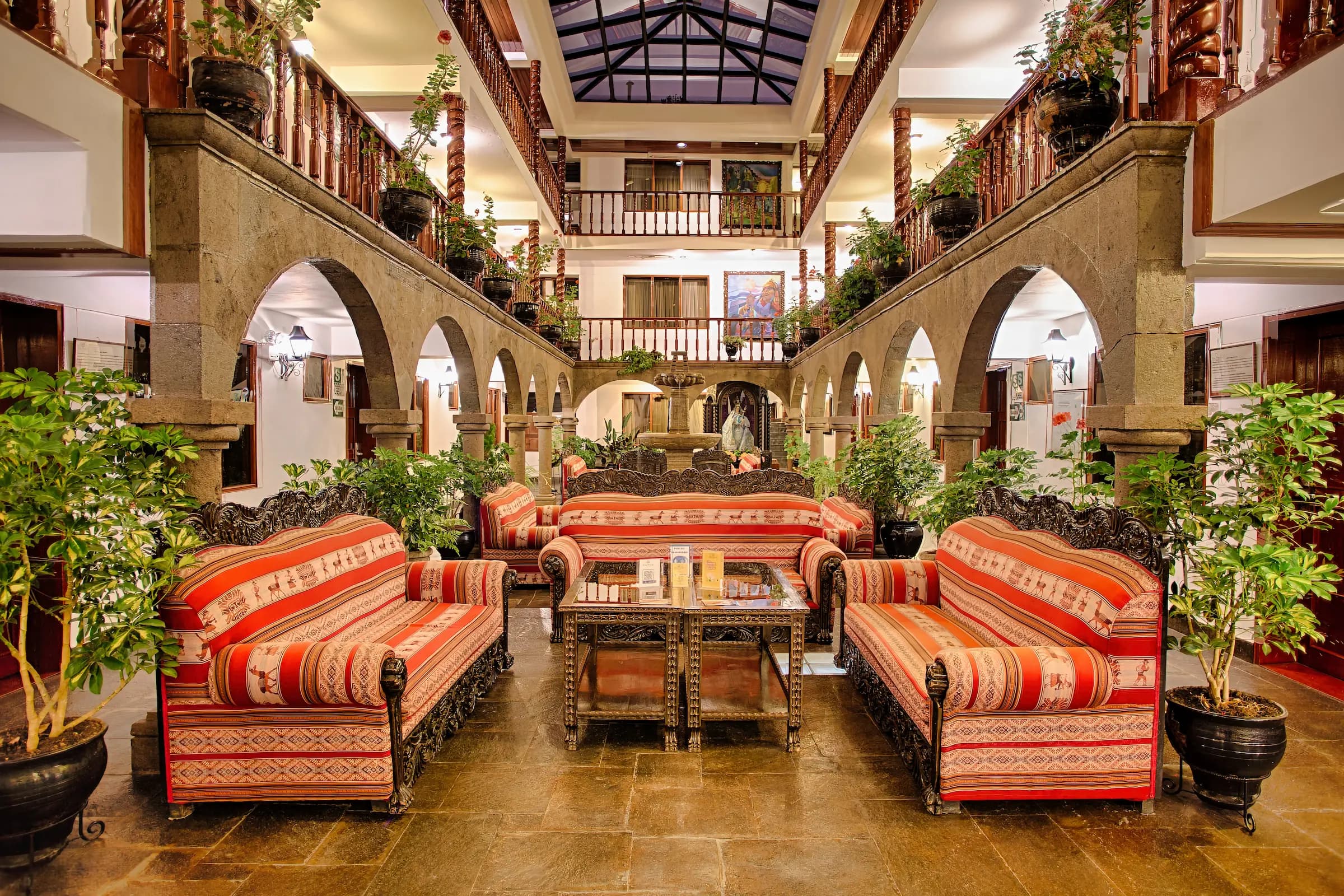 Colonial-style lobby of Munay Wasi Inn featuring ornate wooden furniture, vibrant upholstery, and lush greenery, highlighting modern comforts in a historic setting in Cusco, Peru.