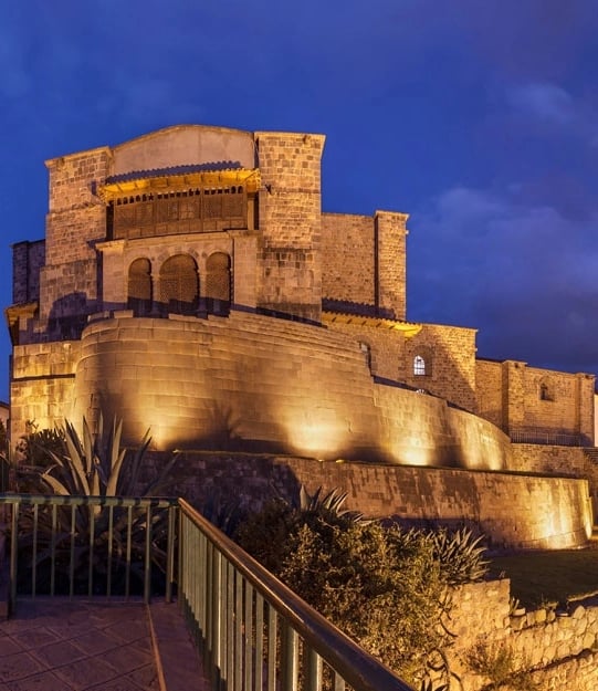 Colonial-style architecture of Qorikancha illuminated at night, showcasing stone walls and traditional design, located in Cusco, Peru, near Munay Wasi Inn.